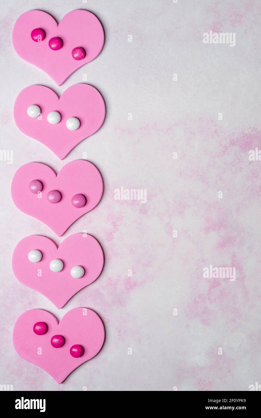 semplice tema giovanile valentino verticale per con cuore in schiuma rosa ritagli con cioccolatini ricoperti di caramelle su sfondo marmorizzato Foto Stock