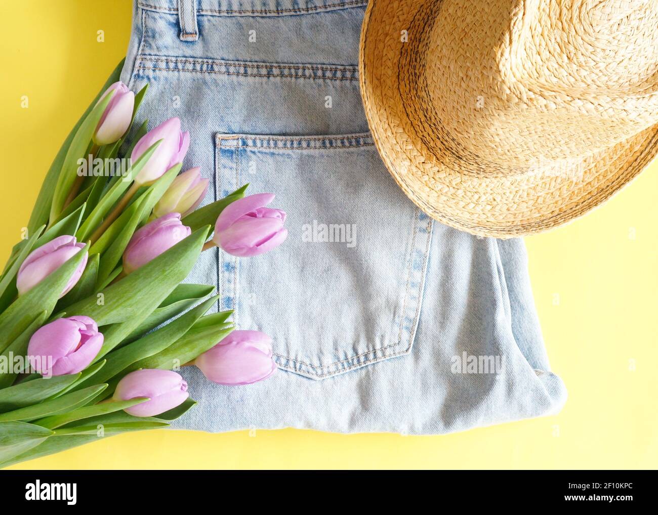 Jeans blu, cappello estivo e tulipani viola fiori su sfondo giallo spazio copia Foto Stock