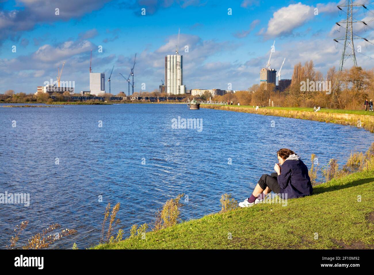 Persona che illumina una sigaretta, smottando e seduto vicino al lago artificiale di Warwick orientale, Walthamstow Wetlands, Lea Valley Country Park, Londra, Regno Unito Foto Stock