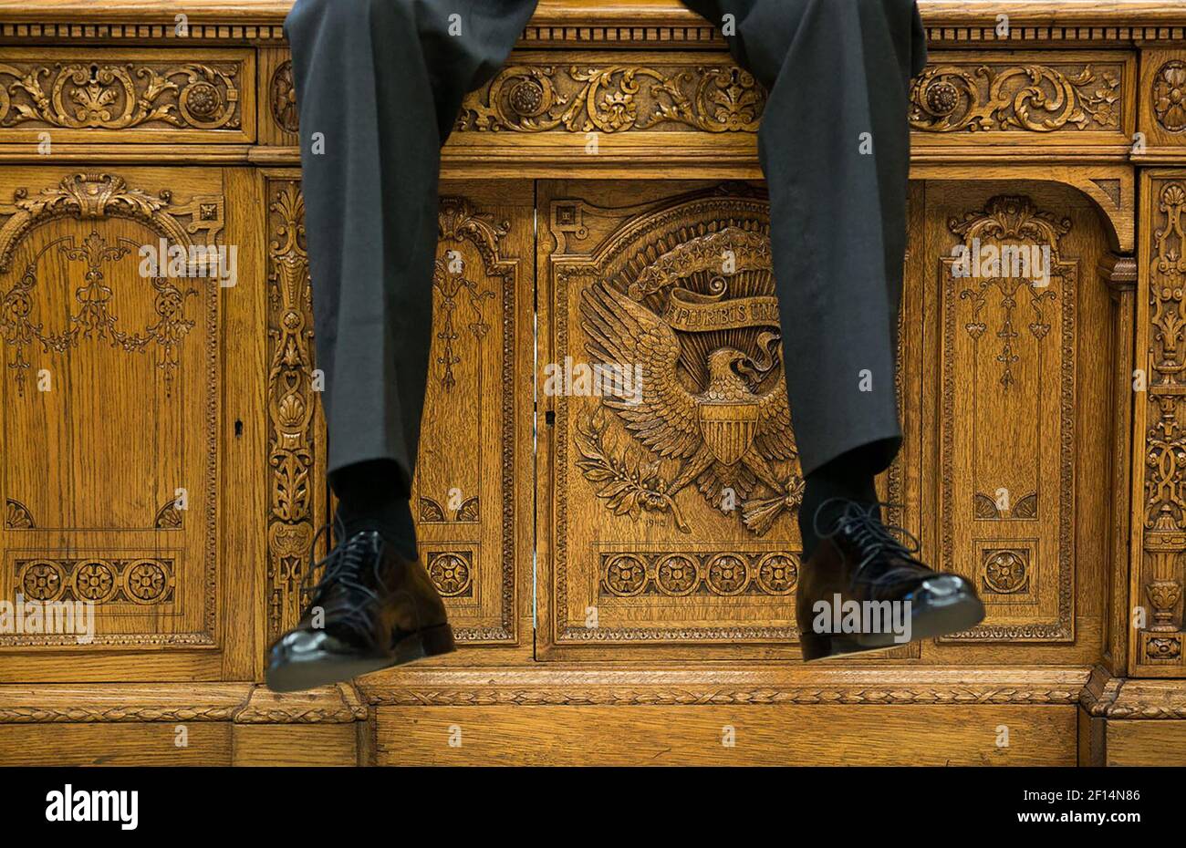 Le gambe del presidente Obama si sono arenate mentre siede sul Resolute Desk, mentre parla con due aiuti nell'ufficio ovale ca. 1° ottobre 2015 Foto Stock