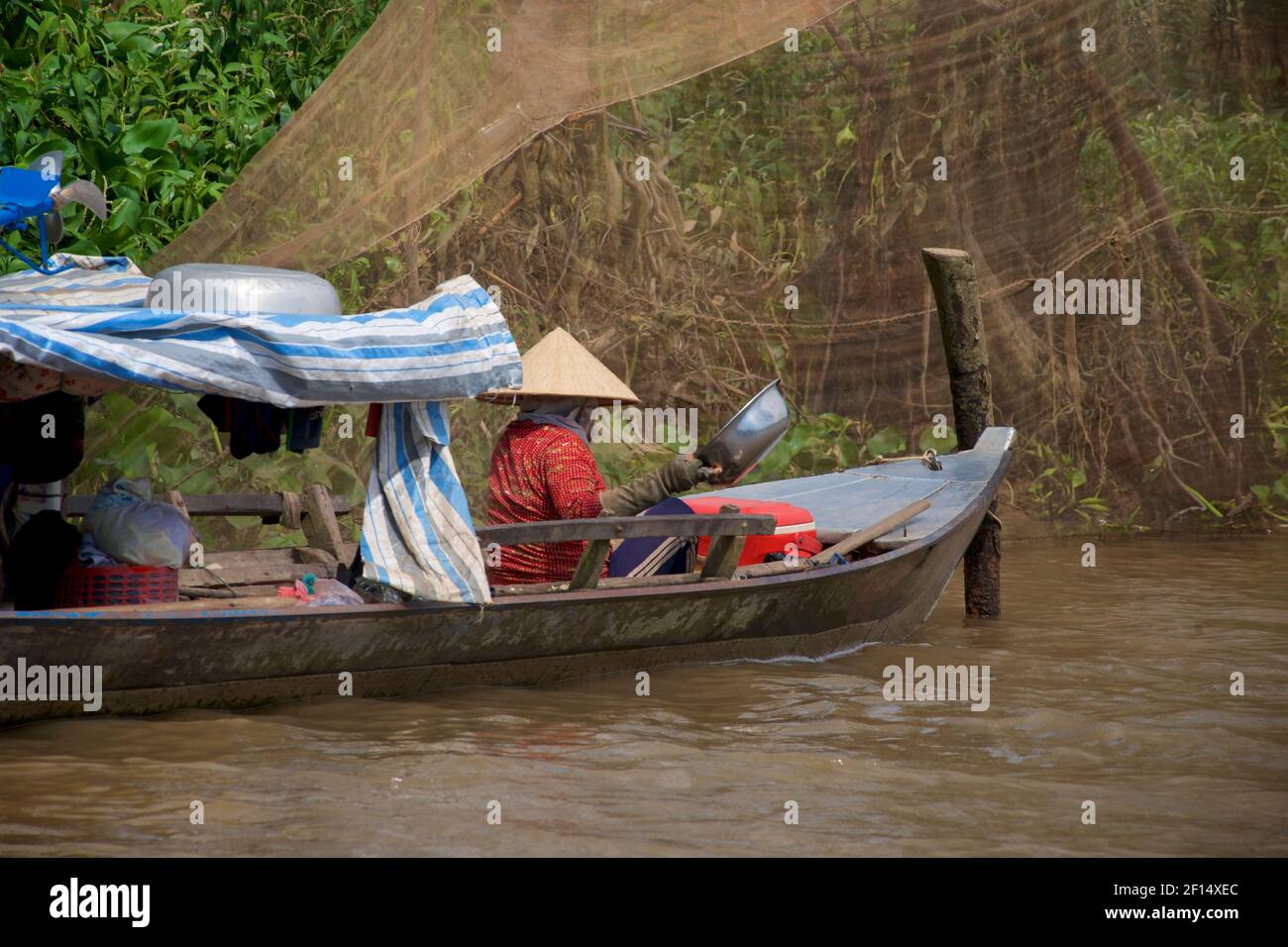 Riverside vita nel delta del Mekong. Distretto di Cat Cai Lậy, Provincia di Tien Giang, Vietnam. Donna vietnamita in cappello conico pesca nei corsi d'acqua del fiume Mekong. Foto Stock