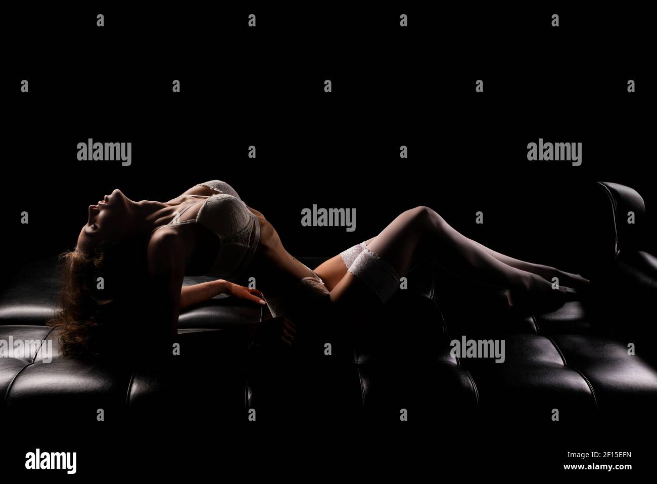 Sensuale giovane donna in intimo sexy giacente al buio divano in pelle Foto Stock