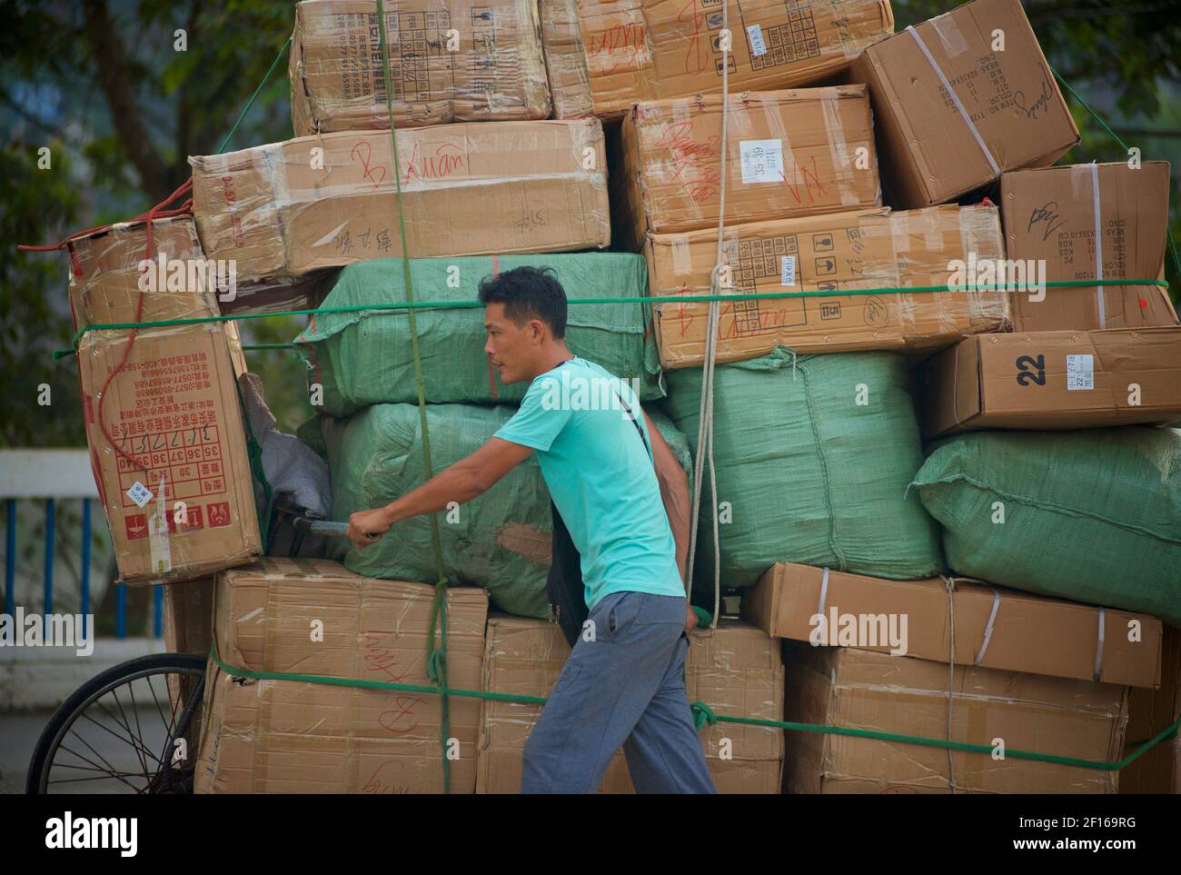 Uomo che trasporta una grande quantità di scatole accatastate in alto sulla sua bicicletta importando attraverso un confine terrestre dalla Cina al Vietnam. Da Hekouzhen a Lao Cai attraverso il ponte di Cau ho Kieu. Foto Stock