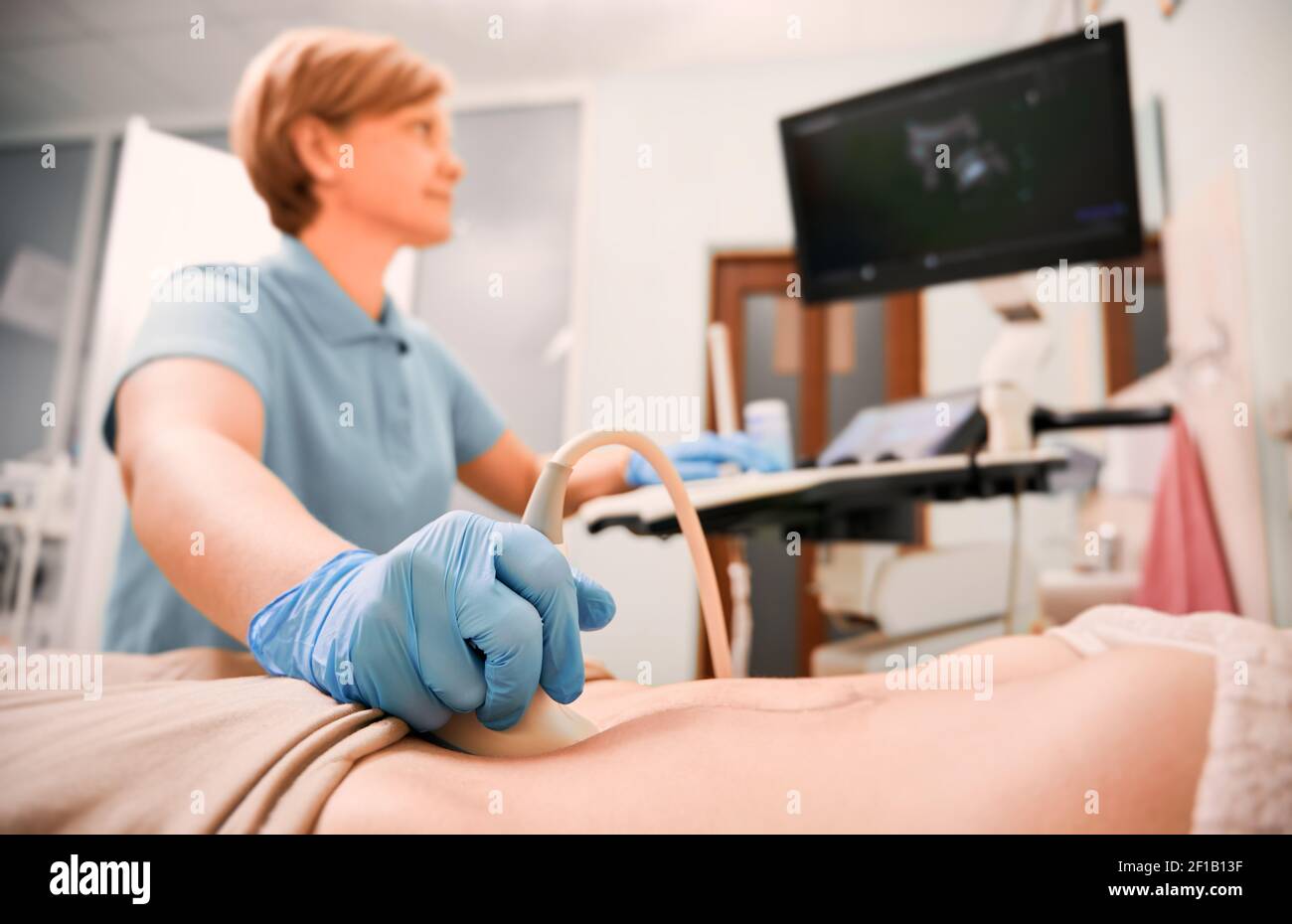 Primo piano della donna che esamina la mano dell'ecografo con lo scanner a ultrasuoni. Trasduttore a ultrasuoni mobile da medico femminile sull'addome del paziente. Concetto di esame medico e diagnostica ecografica. Foto Stock