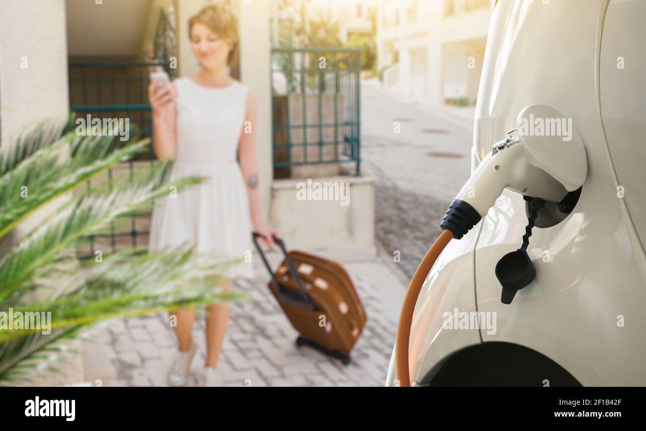 Primo piano della ricarica dell'auto elettrica su uno sfondo di una donna che viaggia con uno smartphone e una borsa Foto Stock