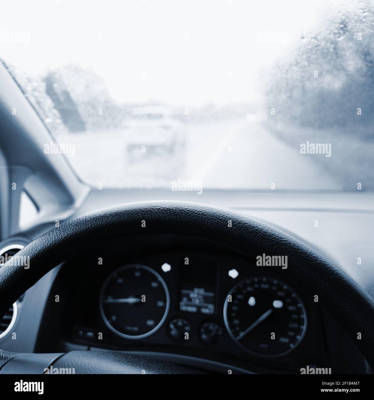 Vista dall'interno del veicolo - conducente con volante e cruscotto. Inverno maltempo piovoso e guida pericolosa su strada. Foto Stock