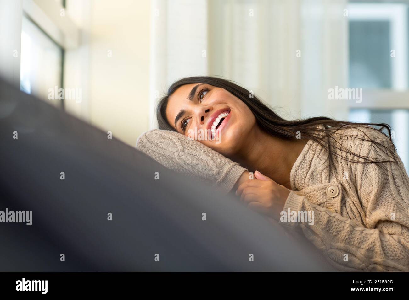 Giovane donna seduta sul divano che guarda fuori dalla finestra Foto Stock