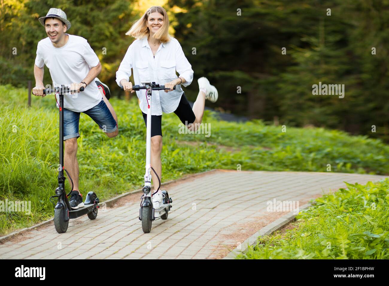 Felice coppia moderna di uomo e donna godendo eco ride in scooter elettrico in giornata di sole in vacanza. Divertirsi insieme guidando uno scooter elettrico attraverso il centro della città. Foto Stock