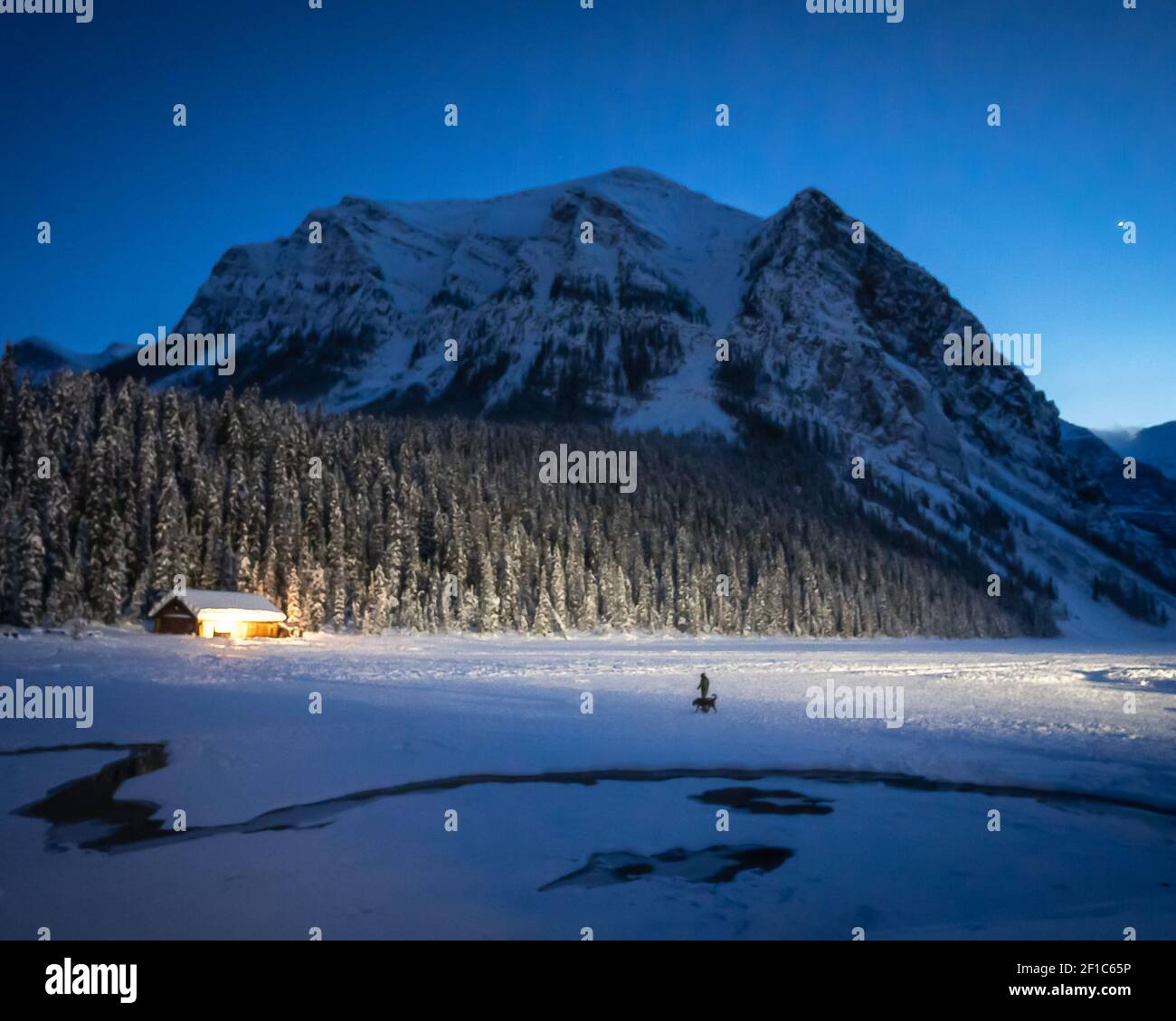 Scena notturna invernale sul lago ghiacciato coperto da neve parzialmente illuminato da una boathouse, girato al lago Louise, Alberta, Canada Foto Stock