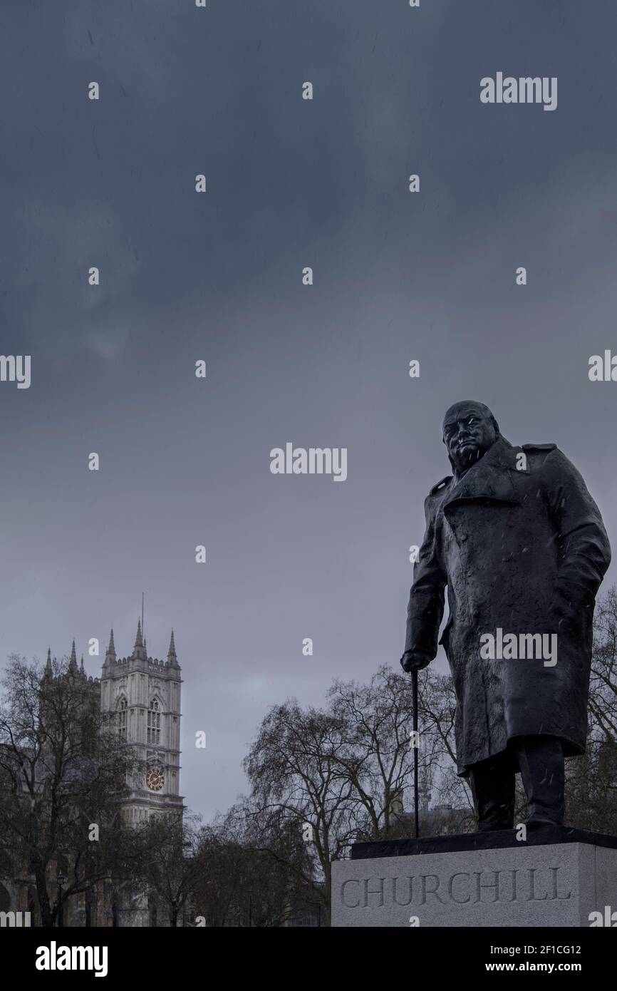 Regno Unito, Londra centrale, Westminster: Statua del primo ministro Winston Churchill in Parliament Square e torri dell'abbazia di Westminster, nuvole pesanti Foto Stock