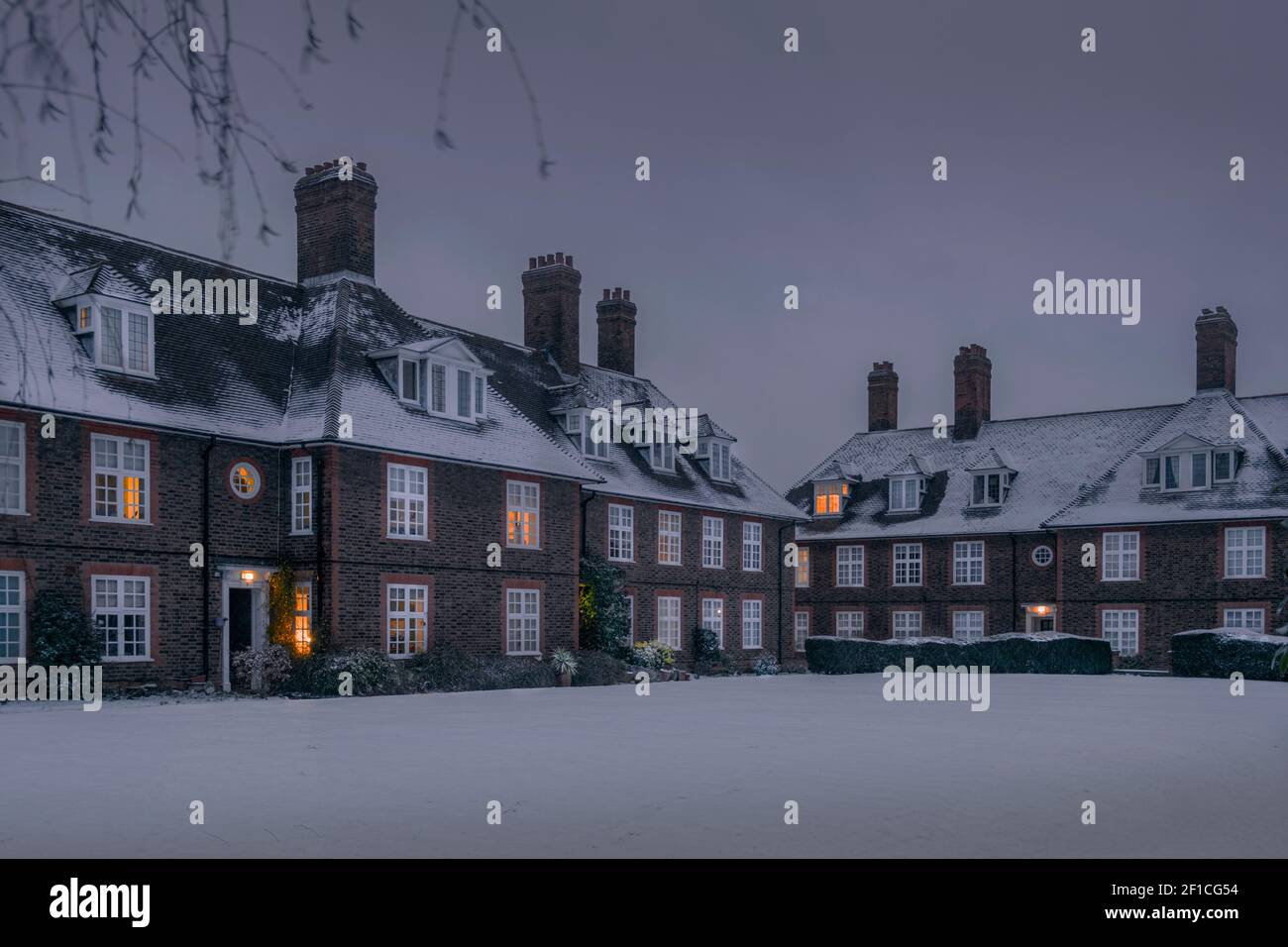 Europa, Regno Unito, Inghilterra, Londra, Barnet, Case cottage a schiera in stile artigianato e arte nel sobborgo di Hampstead Garden. Inverno con neve, caldo bagliore dalle finestre Foto Stock