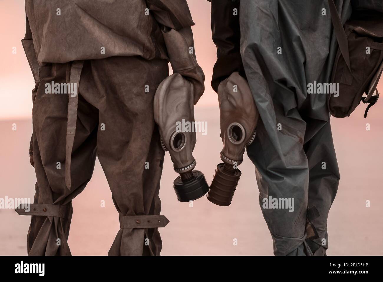 Due persone con maschere a gas e tute di protezione chimica sullo sfondo della terra morta bruciata. Foto Stock