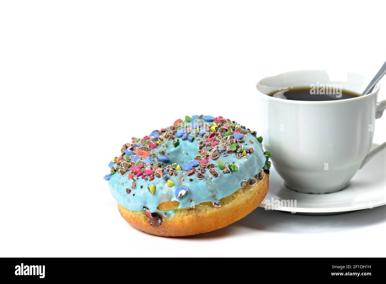 Vista su una ciambella dolce con glassa blu e caramelle schiacciate. Ciambella su sfondo bianco con una tazza di caffè caldo. Piatto dolce. Pronto a mangiare. Arredamento soave Foto Stock