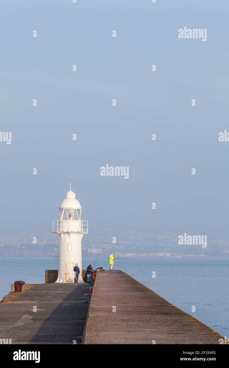 La gente pesca dalla fine del frangiflutti a Brixham vicino al faro Foto Stock