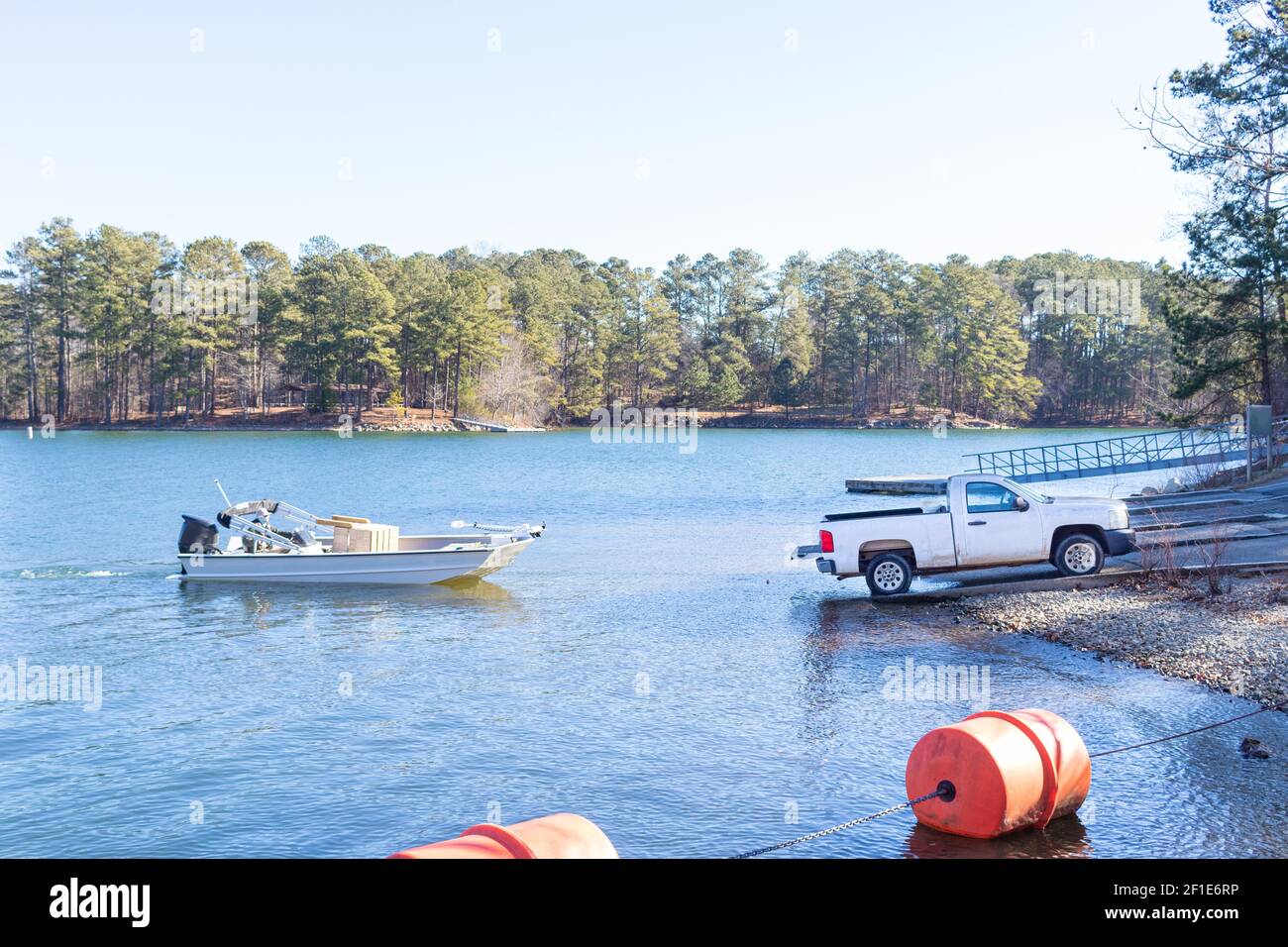 Pick-up camion che tira barca e rimorchio fuori dall'acqua sulla riva di un lago. Foto Stock