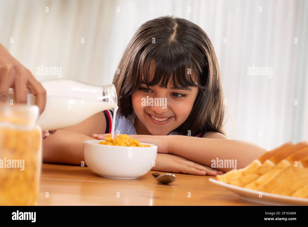 UNA GIOVANE RAGAZZA FELICE IN ATTESA DI MANGIARE CORNFLAKES CON LATTE Foto Stock