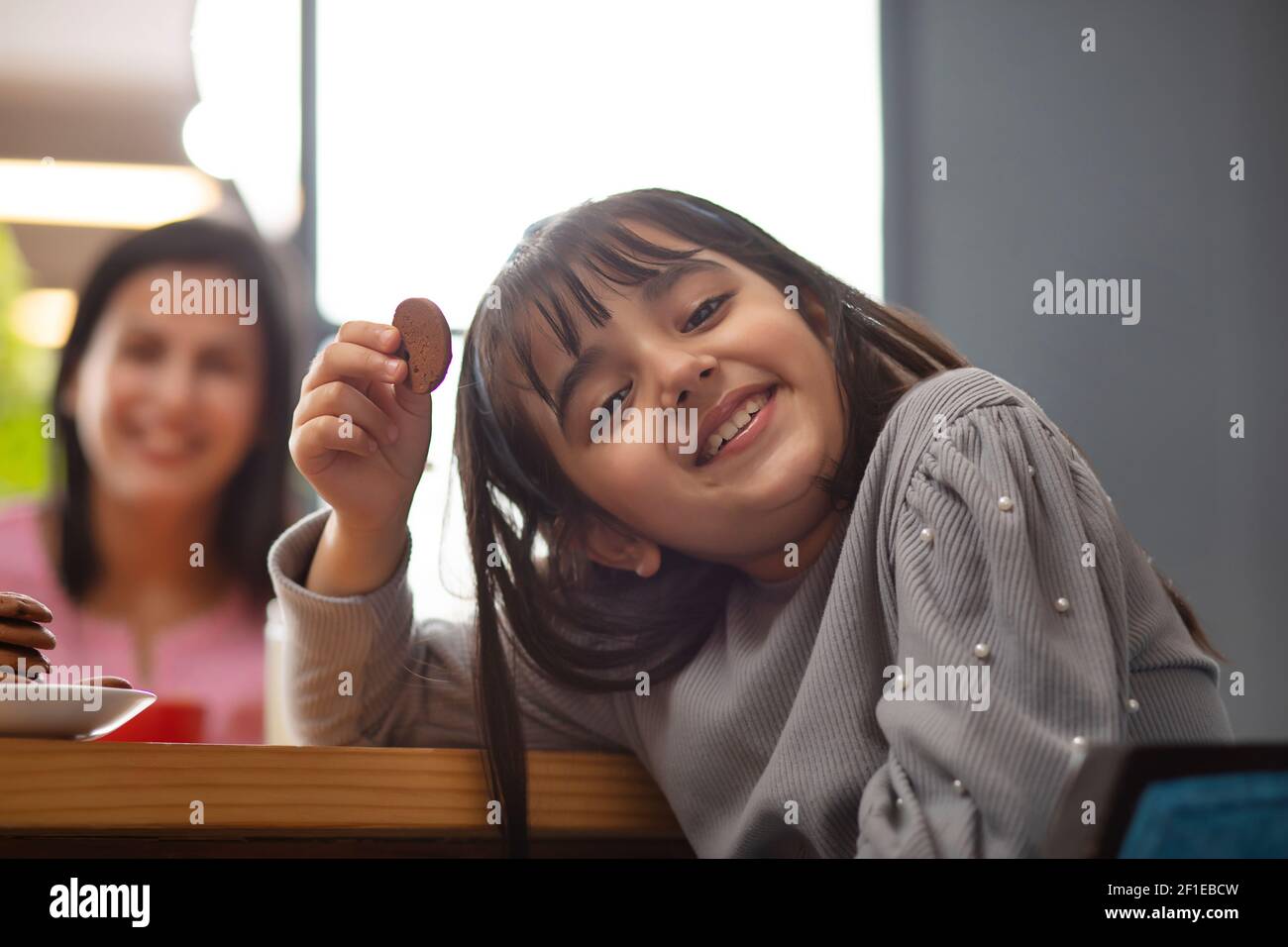 UNA GIOVANE RAGAZZA ALLEGRA CHE GUARDA LA MACCHINA FOTOGRAFICA MENTRE TIENE IL BISCOTTO IN MANO Foto Stock