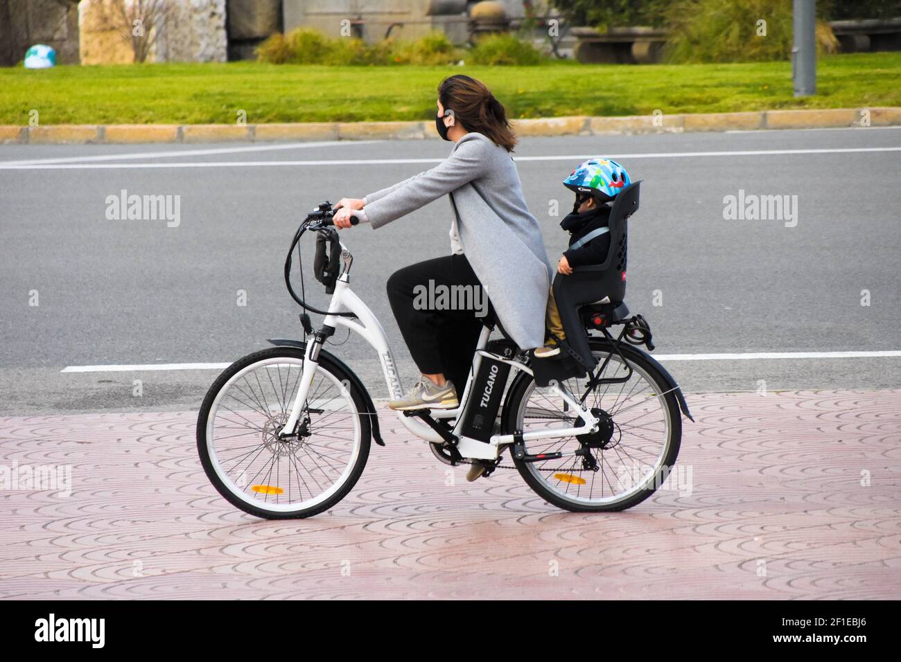 Tutta la lunghezza della madre che pedalano mentre il figlio è seduto sul sedile posteriore del ragazzo.piccolo nella bicicletta del sedile dietro la madre. Bicicletta elettrica, bicicletta elettrica, bicicletta elettrica. Foto Stock