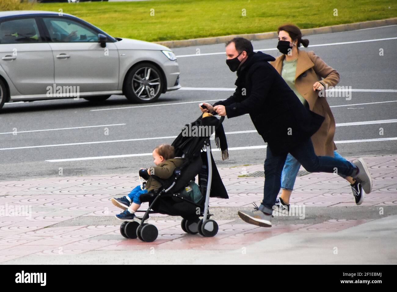 I genitori stressati che spingono un passeggino con il figlio dentro. Sono in esecuzione perché sono in ritardo. Famiglia, stile di vita, momento, tutti i giorni, vita reale. Foto Stock