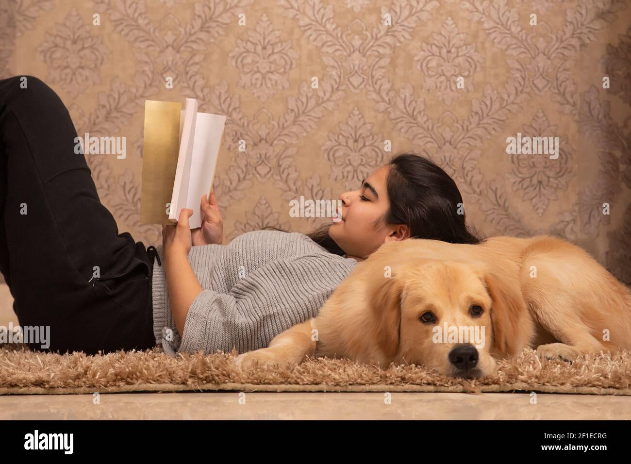 UNA RAGAZZA GIOVANE CHE RIPOSA SUL PAVIMENTO E CHE LEGGE LIBRO CON PET CANE OLTRE Foto Stock