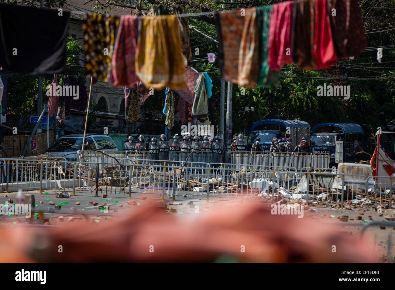 Gli ufficiali di polizia si trovano dietro una barricata improvvisata e longyi, un abbigliamento tradizionale ampiamente indossato in Myanmar, sulla corda attraverso una strada per impedire alla polizia di vedere correttamente durante una manifestazione contro il colpo di stato militare. La polizia del Myanmar ha attaccato i manifestanti con proiettili in gomma, munizioni vive, gas lacrimogeni e bombe stordite in risposta ai manifestanti anti militari contro il colpo di stato lunedì. Due manifestanti sono stati uccisi a Myitkyina, nello Stato di Kachin dalle forze di sicurezza, da fonti locali. Un totale di 1758 persone sono state perseguitate, di cui 1440 ancora nelle prigioni militari del Myanmar e 60 sono state uccise Foto Stock