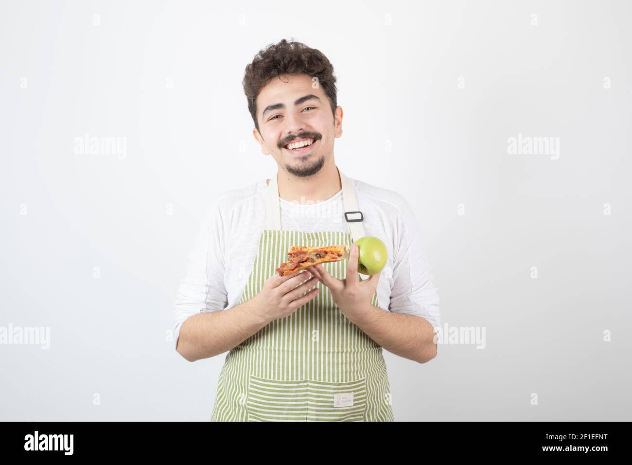 Ritratto del cuoco maschio sorridente che tiene mela e pizza sopra sfondo bianco Foto Stock