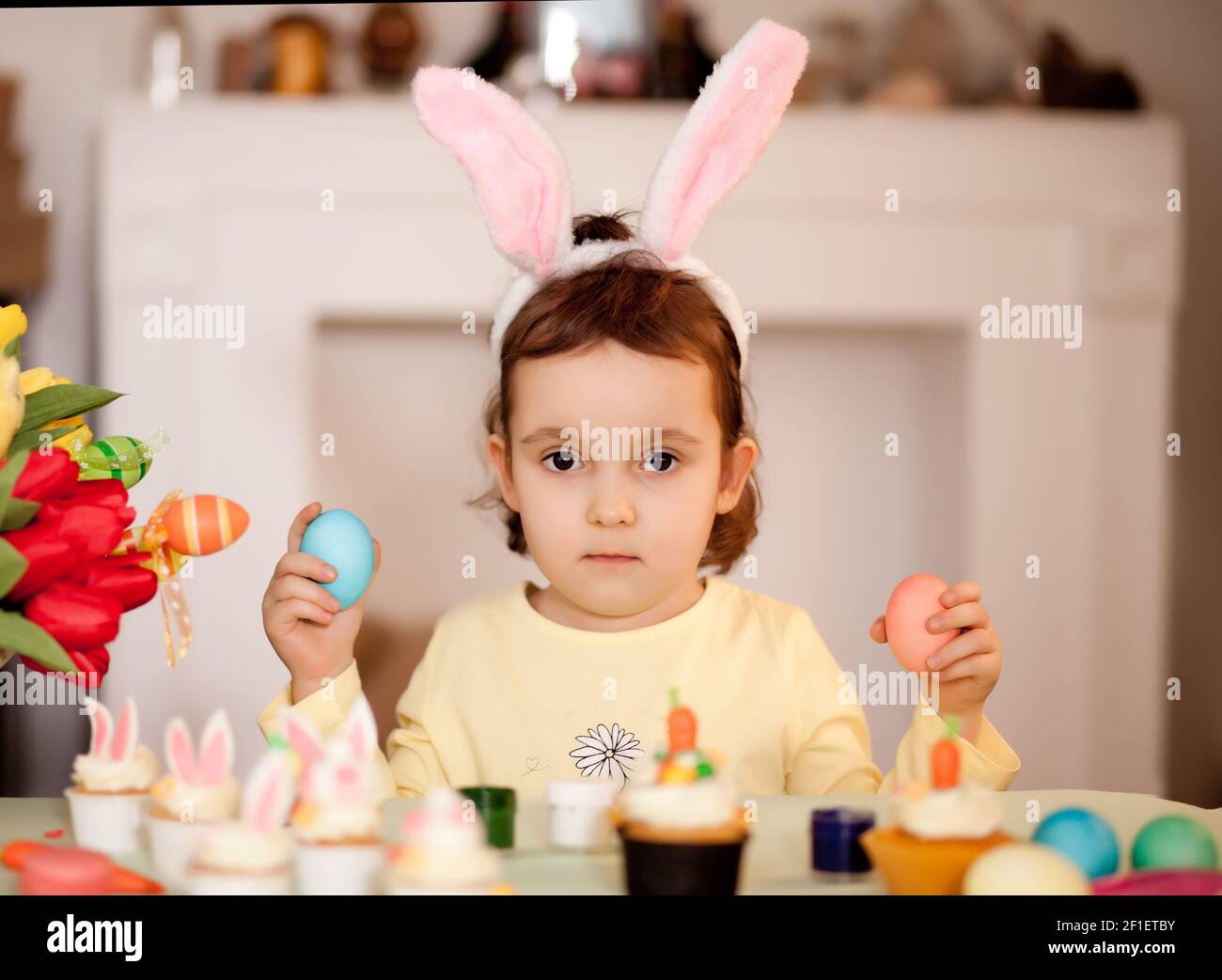 Bambina divertente che indossa orecchie conigliate e con uovo di Pasqua in mano a casa Foto Stock