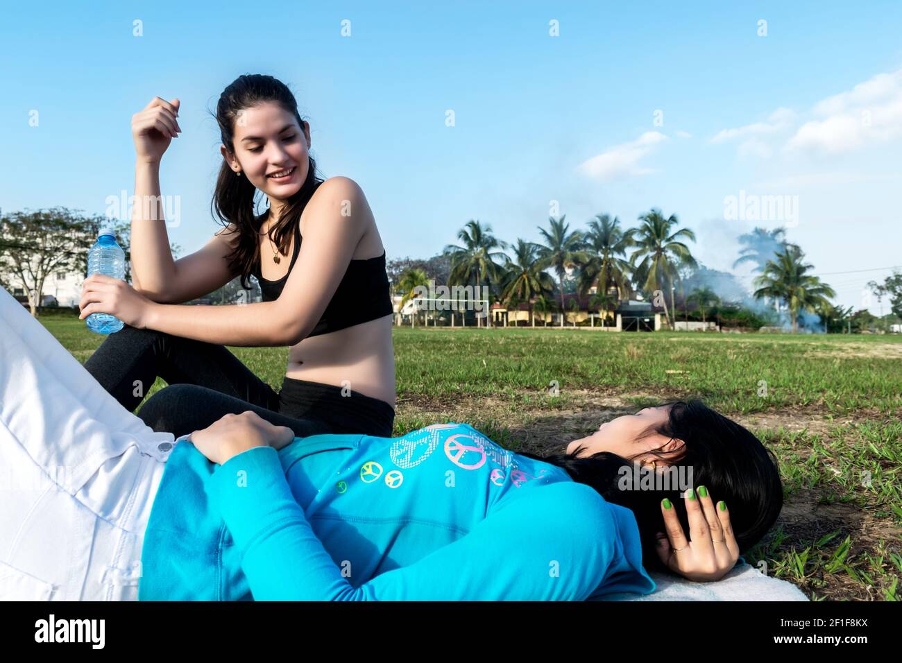 Due giovani donne che si riposano sull'erba e si comunicano tra loro all'aperto a Cuba, una è seduta, l'altra è sdraiata sulla schiena Foto Stock