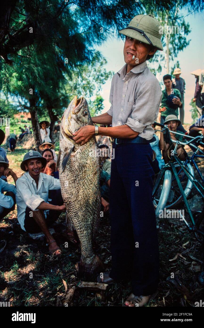 Un pescatore con un grande pesce che ha catturato, villaggio costiero, Vietnam del Nord, giugno 1980 Foto Stock