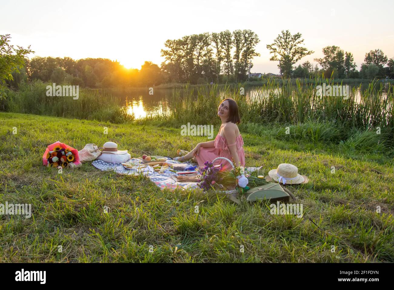 Una giovane donna si siede su un picnic in un parco sulle rive di un fiume Foto Stock