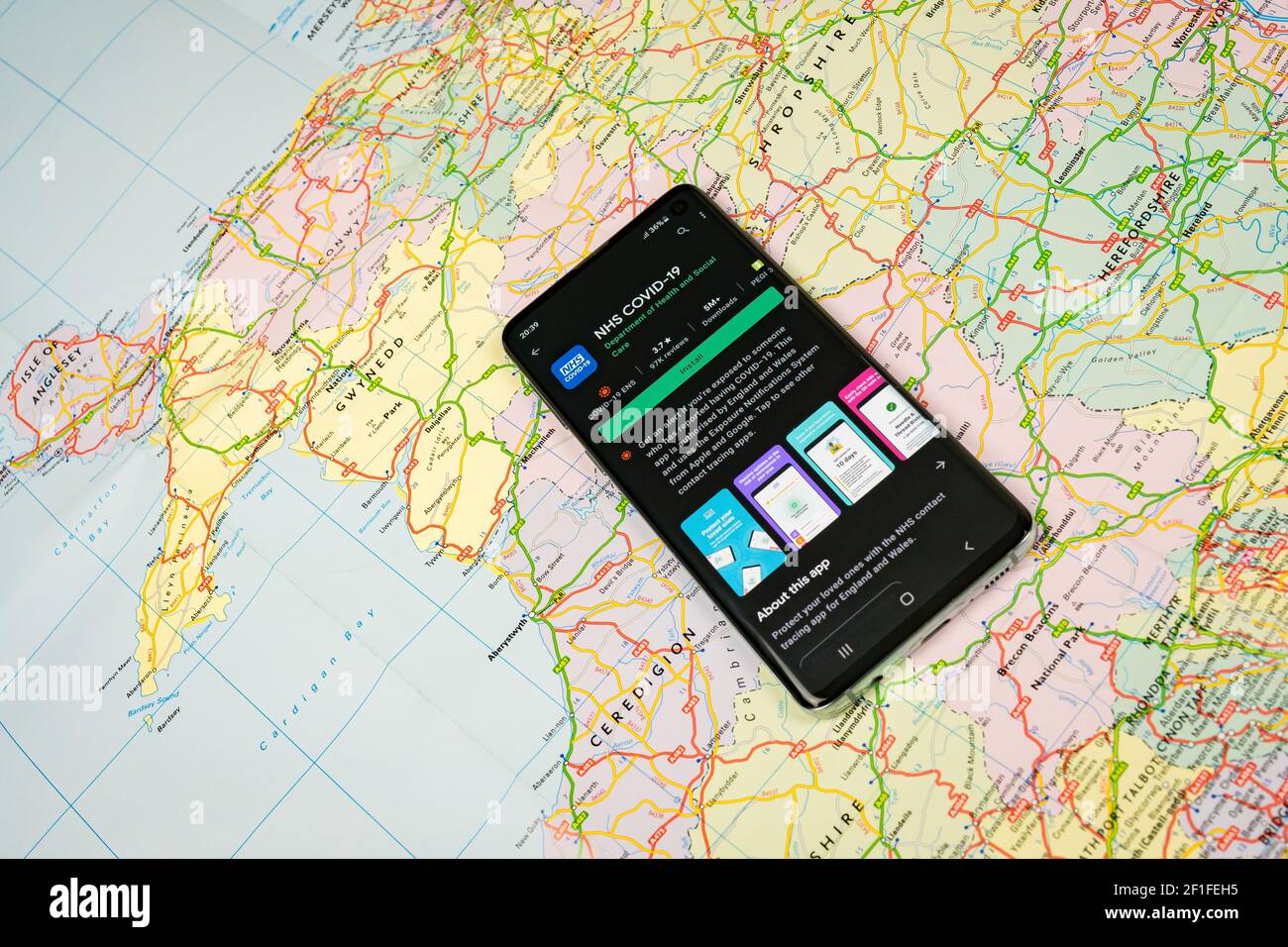 Smartphone con app NHS COVID-19, app National Health Service, visualizzata su Google Play con mappa del Regno Unito e maschera facciale sullo sfondo Foto Stock