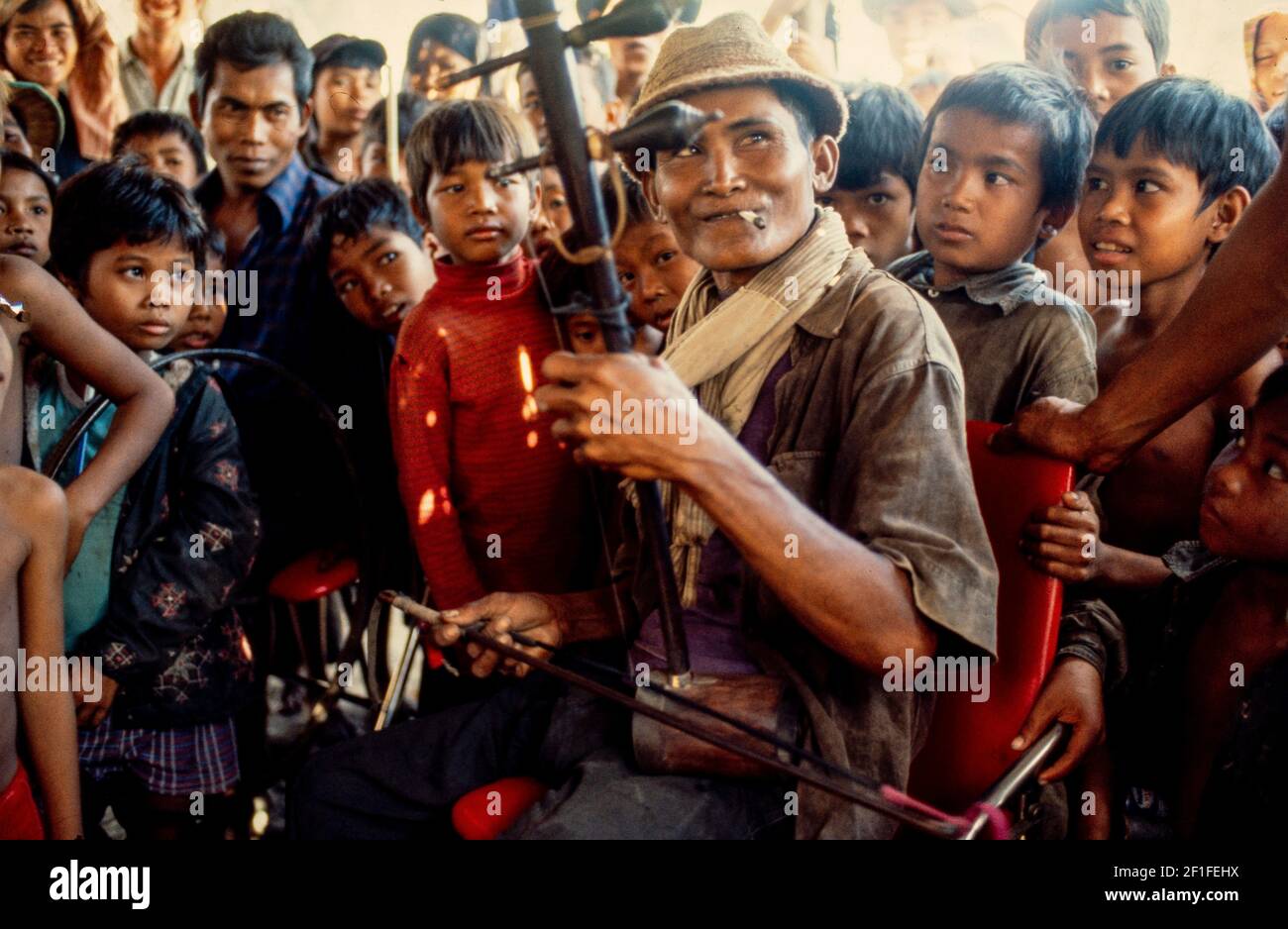 Un musicista con un tradizionale strumento a due corde Dan Nhi che intrattiene i bambini per strada, ho Chi Minh City, Vietnam, giugno 1980 Foto Stock