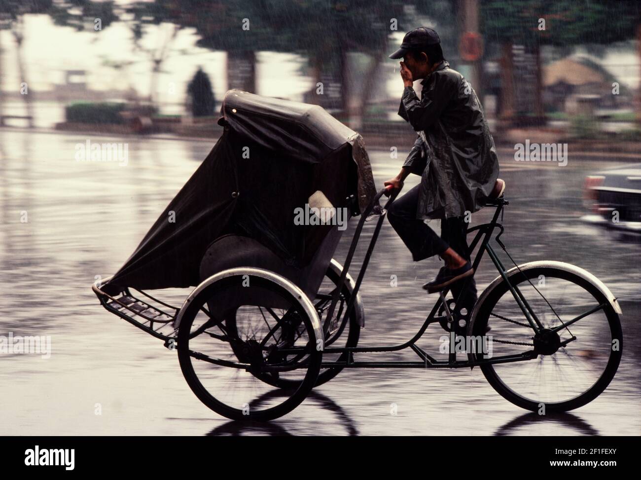 Un driver del ciclo del pedel durante una pioggia monsonica, ho Chi Minh City, Vietnam, 1980 giugno Foto Stock