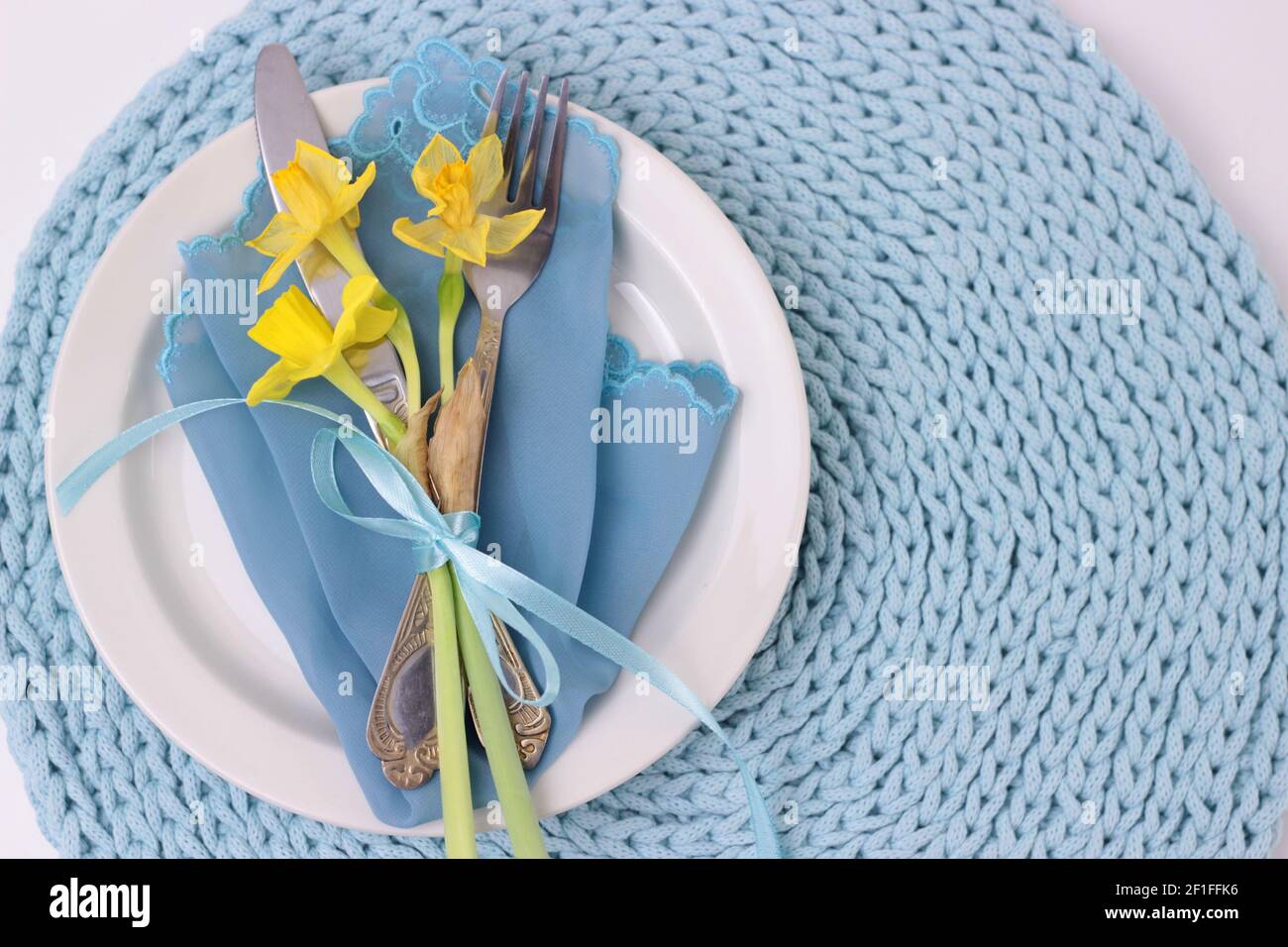 Bella vacanza di Pasqua tavolo con posate. Fiori di Narcissus, utensili da cucina con prua su piastra bianca. Tessuto di colore acqua sfondo tovagliolo, Foto Stock