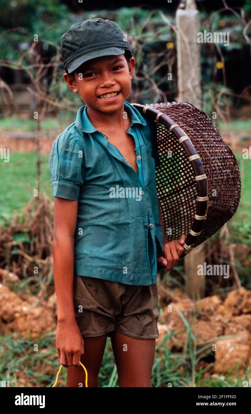 Un ragazzo con il suo cesto di pesce che va a caccia di granchi nella risaia, nel sud del Vietnam rurale, giugno 1980 Foto Stock