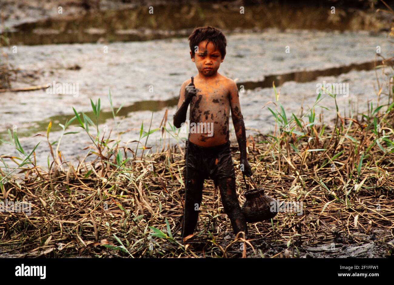 Un ragazzo nel fango profondo della risata della sua famiglia a caccia di granchi, rurale del sud del Vietnam, giugno 1980 Foto Stock