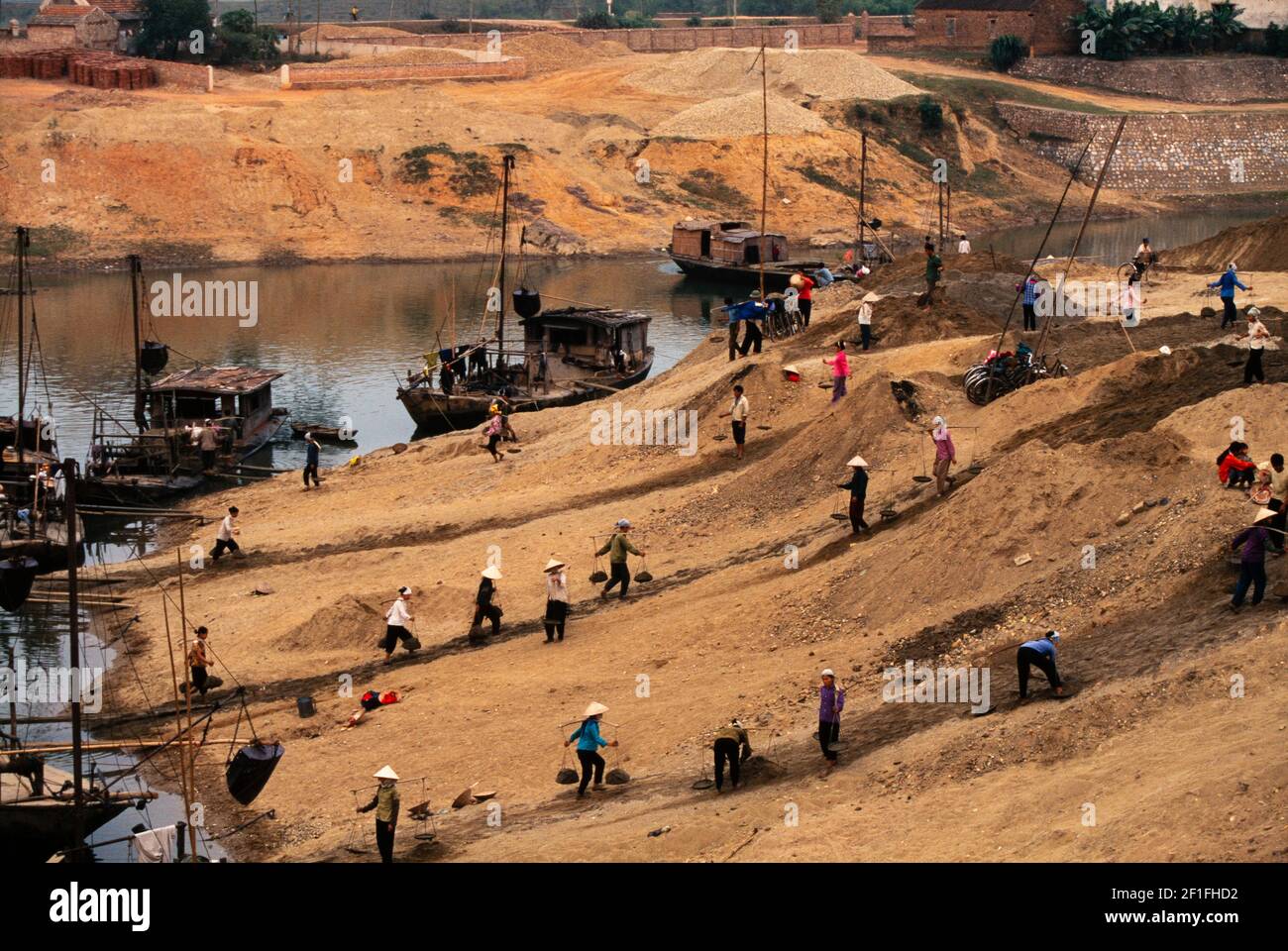 Lavoratori che trasportano materiali da costruzione da chiatte fluviali per una nuova costruzione sulla riva del fiume, rurale sud Vietnam, ottobre 1995 Foto Stock