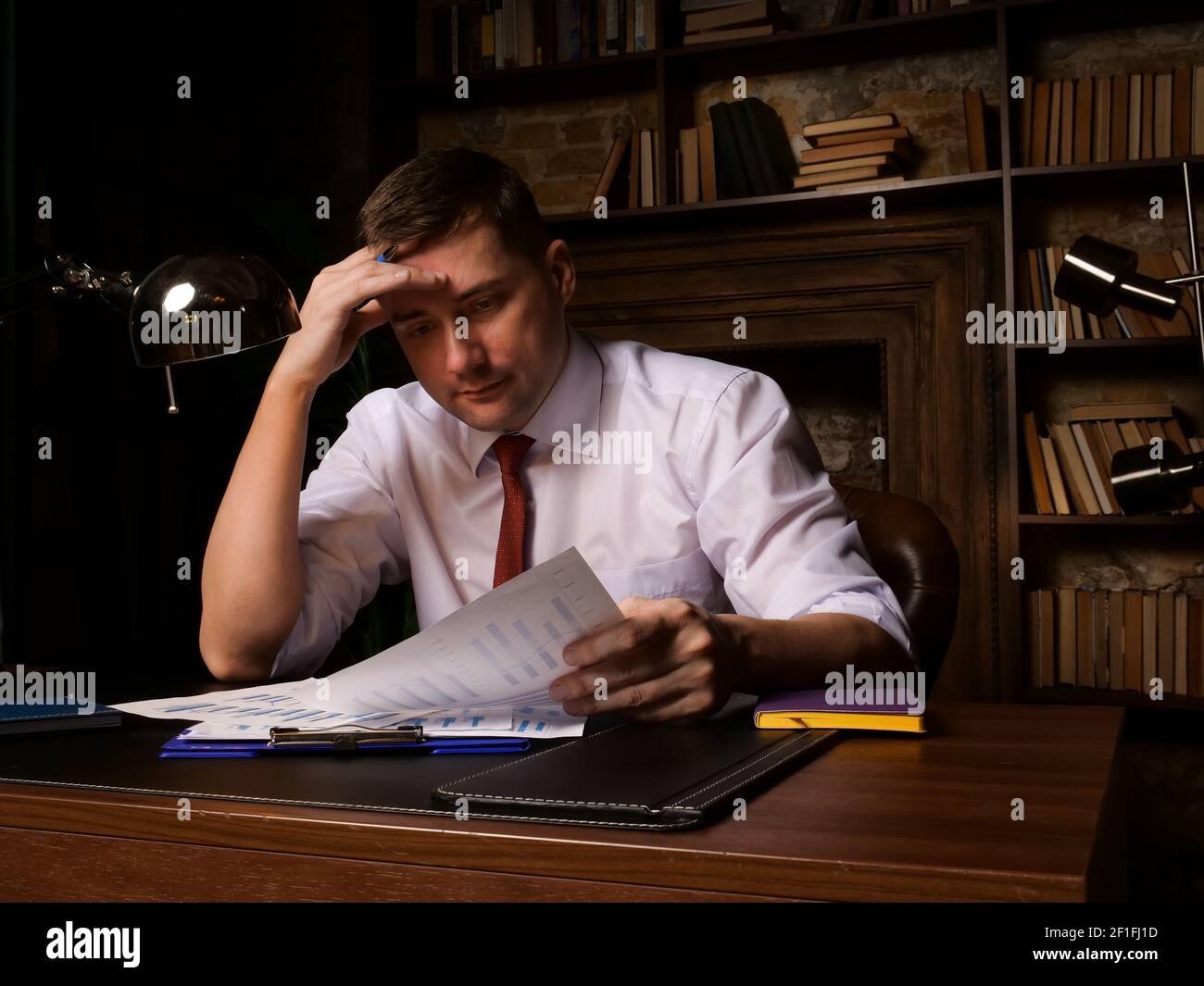 Un dipendente stanco o un uomo d'affari lavora con documenti a tarda notte. Foto Stock