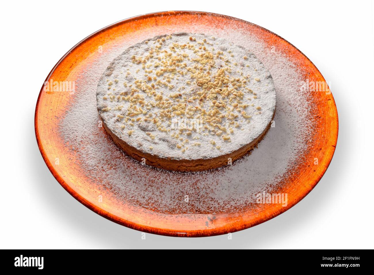 torta di nocciole con zucchero a velo e nocciole tritate in arancio piastra isolata sul bianco Foto Stock