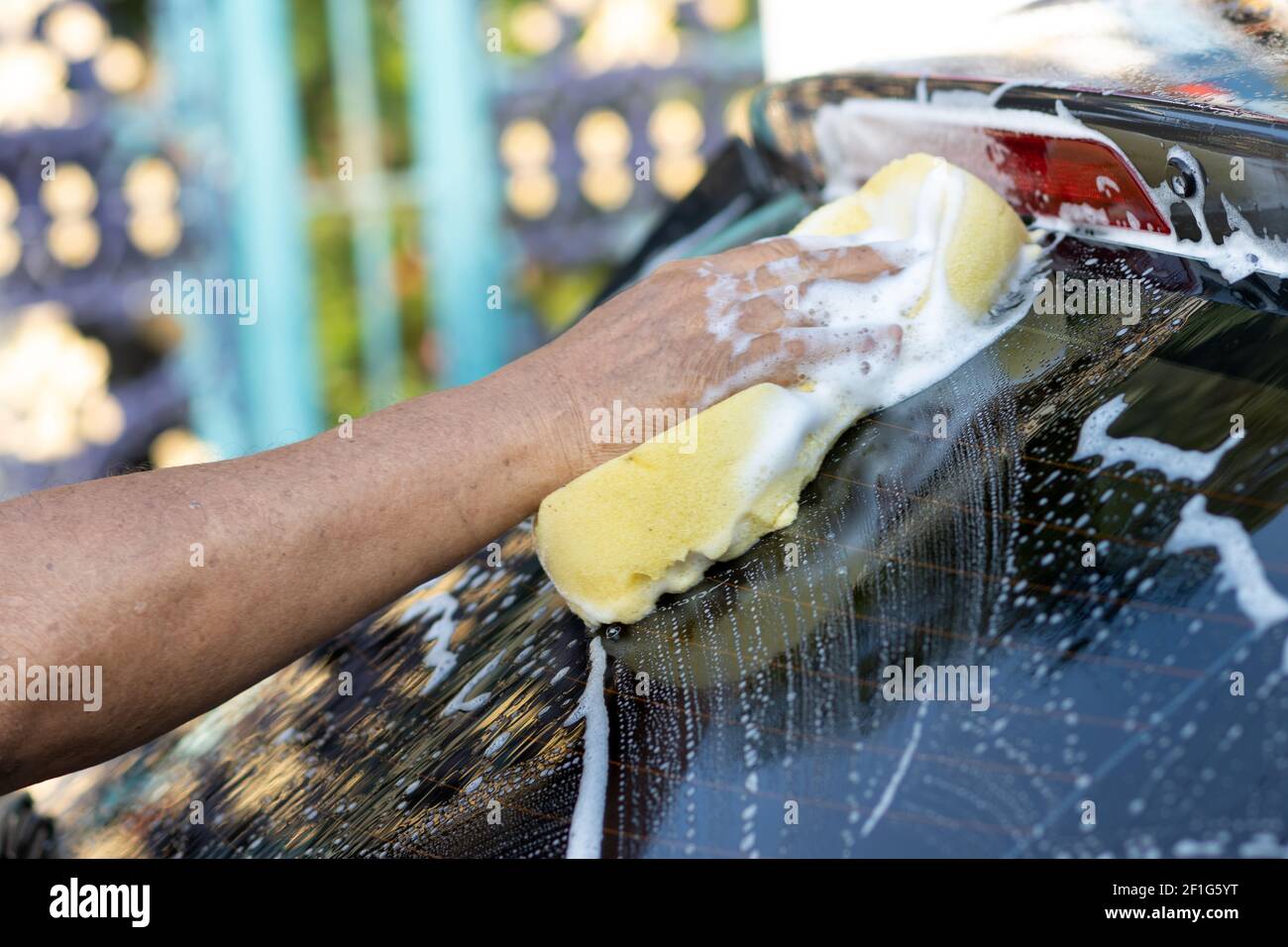 Lavarsi a mano con acqua saponata. L'uomo pulisce l'auto con spugna, acqua e detergente. Foto Stock