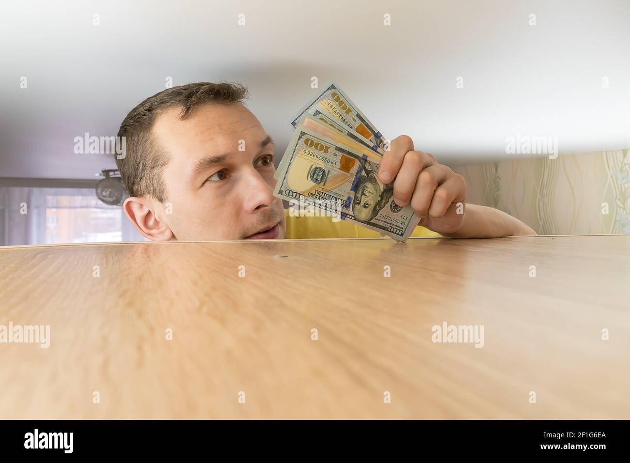 L'uomo tiene il risparmio del dollaro nascosto su un armadietto nelle sue mani. Risparmio di denaro in tempi difficili Foto Stock