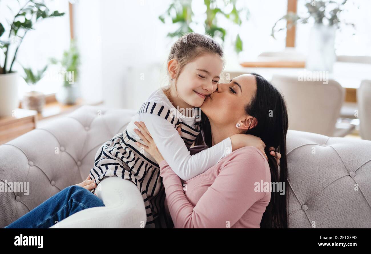 Madre con piccola figlia seduta sul divano all'interno di casa, baciando. Foto Stock