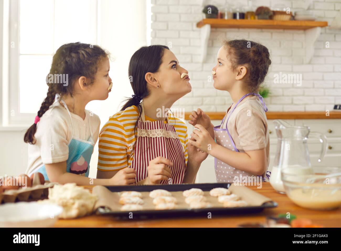 Mamma e figlie giocose fanno biscotti e si divertono a fare baffi fuori dall'impasto. Foto Stock