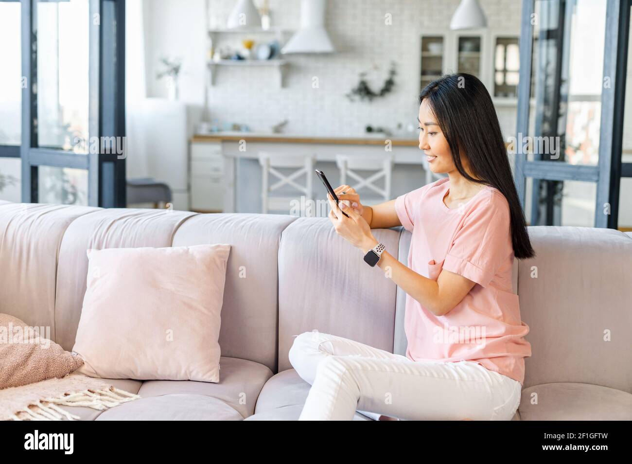 Bella donna asiatica con lunghi capelli neri, seduta sul divano, guardando  il cellulare, videochiamata, testando, parlando