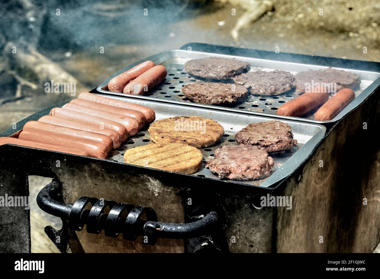 Colpo orizzontale di hamburger e hot dog che cucinano su una griglia all'aperto. Foto Stock