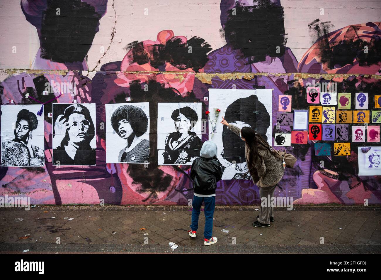 Madrid, Spagna. 8 Marzo 2021. Una donna mostra al figlio un murale femminista che è apparso oggi vandalizzato durante la Giornata Internazionale della Donna. I cartelli delle donne sono stati posti sopra i dipinti dopo che il murale è stato vandalizzato con vernice nera. Il murale rappresenta donne famose di tutto il mondo, con i volti di 15 donne che fanno parte della storia per la loro lotta a favore dell'uguaglianza: Credit: Marcos del Mazo/Alamy Live News Foto Stock