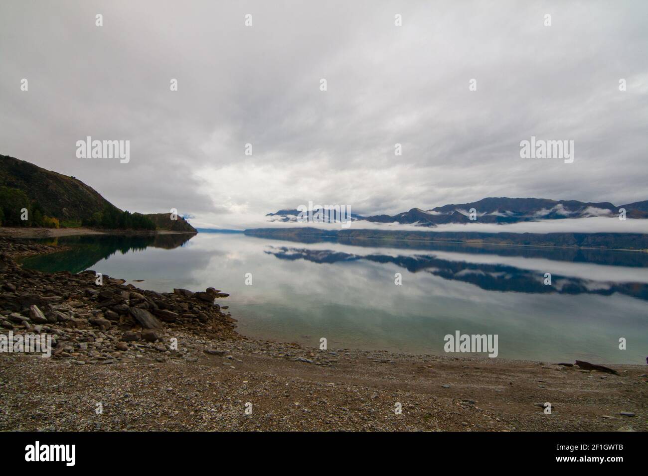 Lago Hawea, Isola del Sud della Nuova Zelanda. Vista incontaminata attraverso l'acqua blu che riflette le nuvole e la nebbia di montagna Foto Stock
