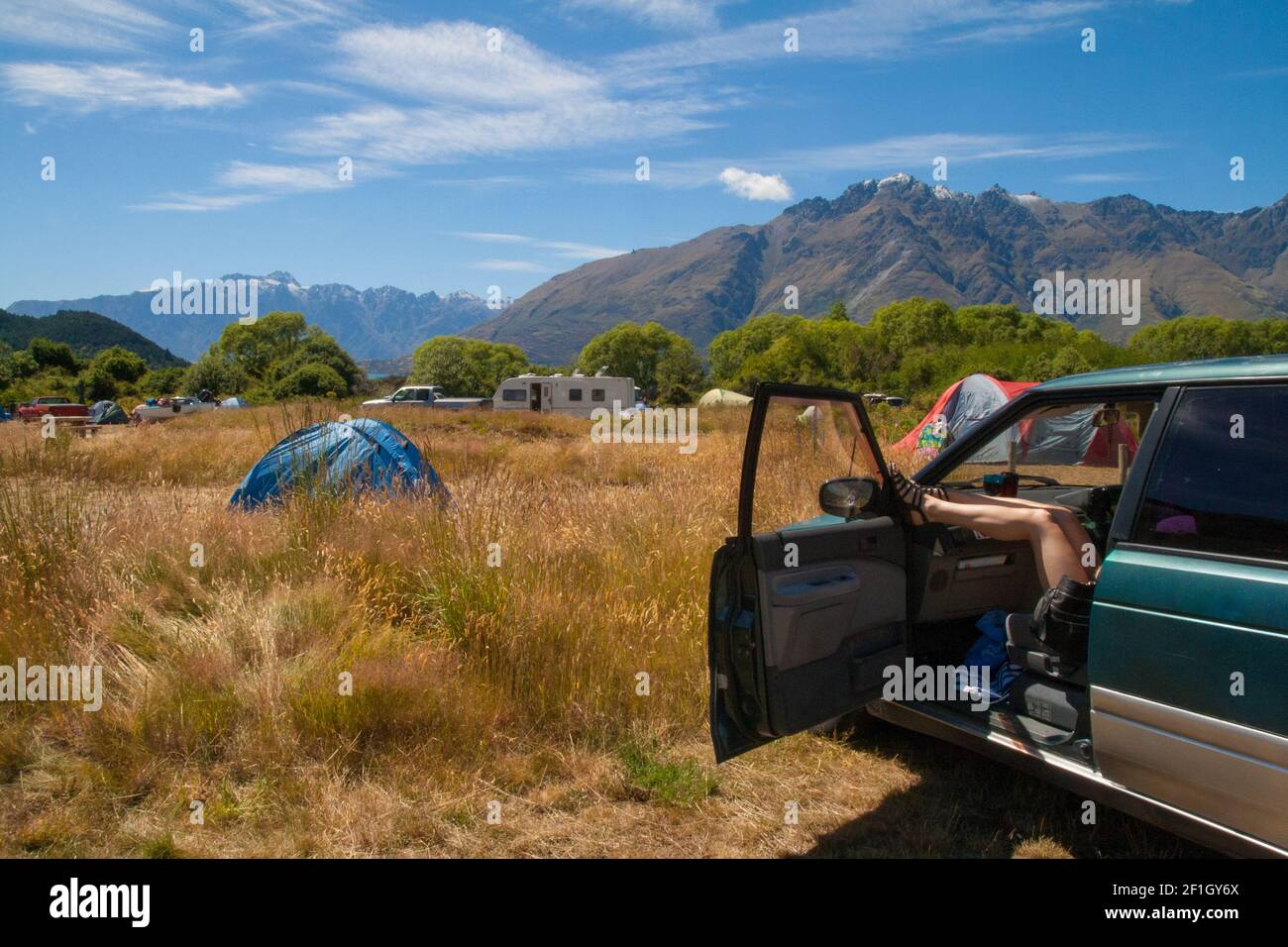 Donna che riposa le gambe attaccando fuori dell'automobile con le porte aperte ad un campeggio vicino a Queenstown, la Nuova Zelanda libertà di campeggio e di viaggiare stile di vita Foto Stock