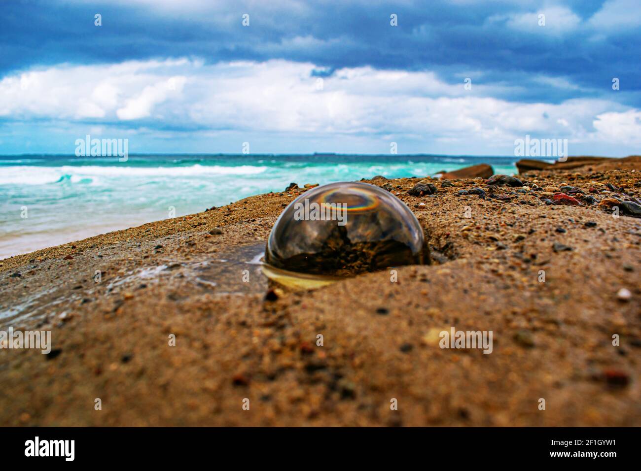 Una palla di cristallo scuro con il riflesso appena visibile della spiaggia sabbiosa, del mare e del cielo nuvoloso Foto Stock