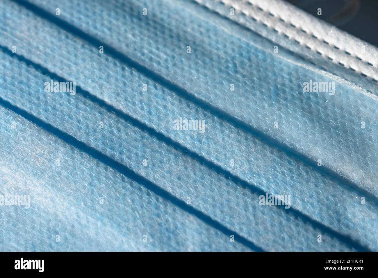 Primo piano della superficie blu frontale di una maschera medica o chirurgica. Articolo monouso realizzato dall'uomo con dispositivi di protezione individuale, struttura in plastica. Foto Stock